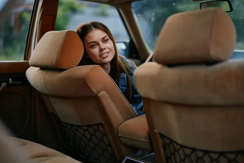 Young woman smiling in a vintage car interior, showcasing casual fashion and warm tones, evoking nostalgia and comfort.