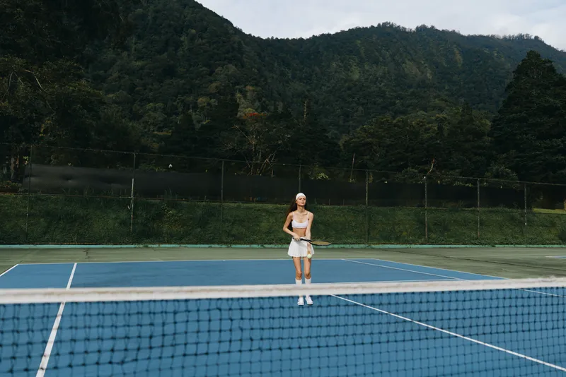 Young female tennis player in a casual sports outfit on a blue tennis court, showcasing determination and focus amid a lush green backdrop