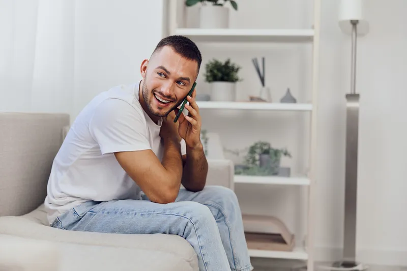 Happy man engaged in a heartfelt phone conversation, expressing connection and vulnerability in a cozy home environment, embodying modern emotional minimalism.