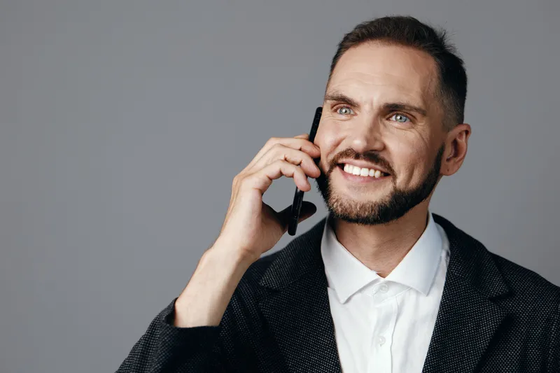 Professional business man speaks on a phone against a colored isolated background, his confident smile and relaxed posture convey seriousness with approachability and strong leadership.