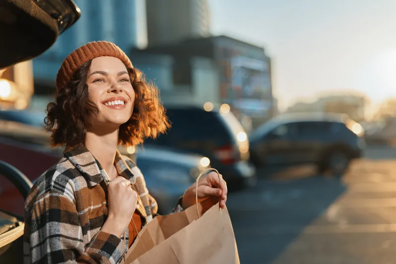 Woman smile shopping by car in parking lot, city sunlight and happiness captured with authenticity, candid lifestyle and golden hour glow, mindful living and emotional storytelling.