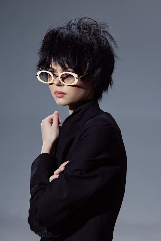 Stylish woman wearing white sunglasses and black clothing with a modern haircut and serious expression