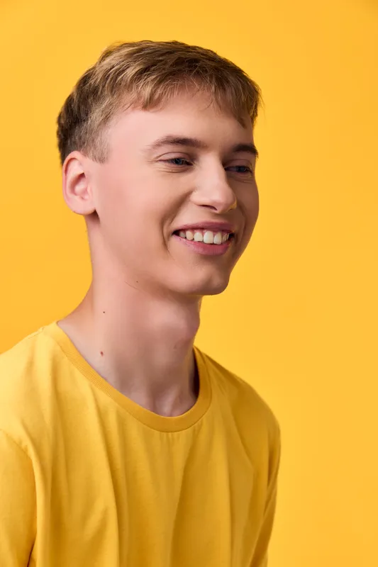 Happy, smiling male in a yellow tee against a bright yellow studio backdrop, close-up shot highlighting cheerful mood and bold color for lifestyle and fashion use