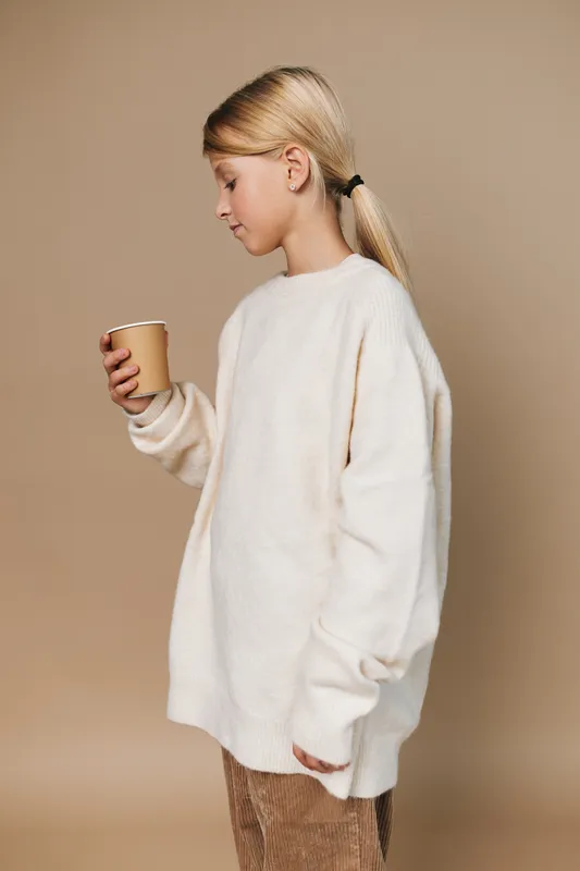 Authenticity shines as a young girl in a cozy sweater holds a cup, capturing a candid lifestyle moment in a simple school themed setting.