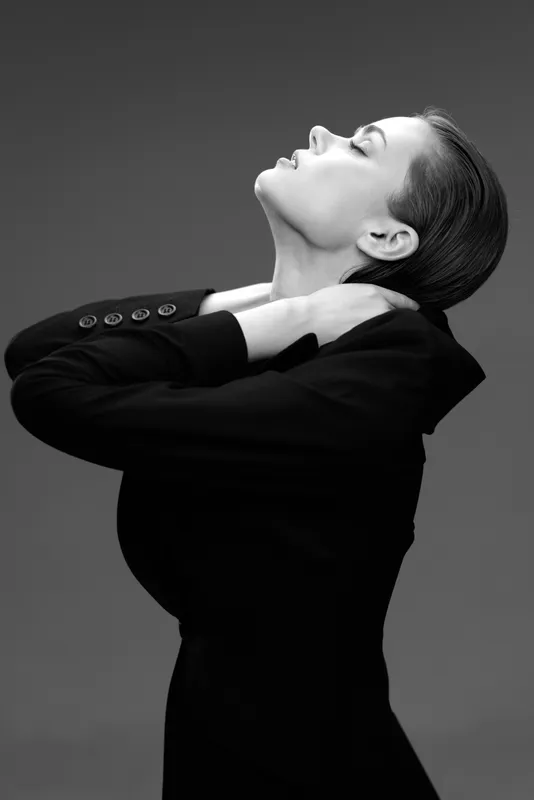 Elegant woman in black jacket with closed eyes posing in black and white portrait with dramatic lighting and smooth background