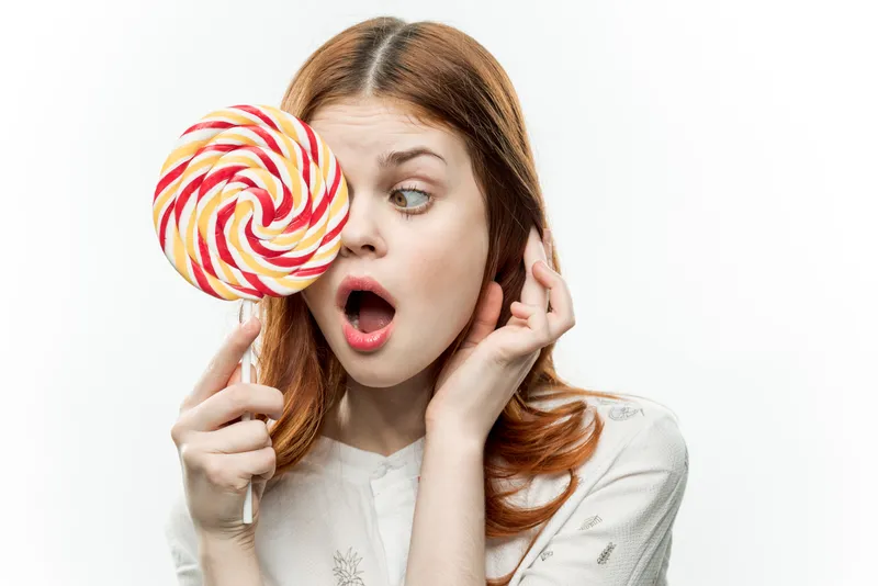 Женщина держит разноцветный леденец у лица, кадрированный вид, эмоция с открытым ртом