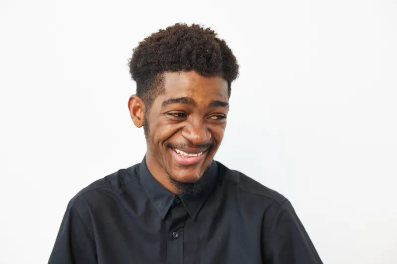 A joyful black man smiling, wearing a stylish black shirt. His expression radiates positivity and confidence, perfect for diverse projects and campaigns.