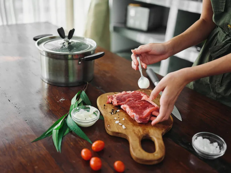 Женщина на кухне готовит ужин из мяса, овощей и специй на деревянном столе на фоне стильной кухни, крупный план рук, свежие экопродукты, образ жизни