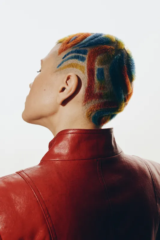 woman with colorful shaved hairstyle wearing red leather jacket, creative fashion look, artistic expression, short hair, vibrant colors, studio lighting