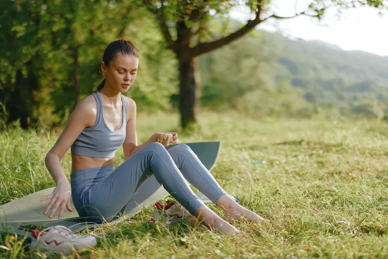 Young female model in activewear sitting on a surfboard in a sunny outdoor setting, reflecting a vibrant lifestyle and a connection with nature