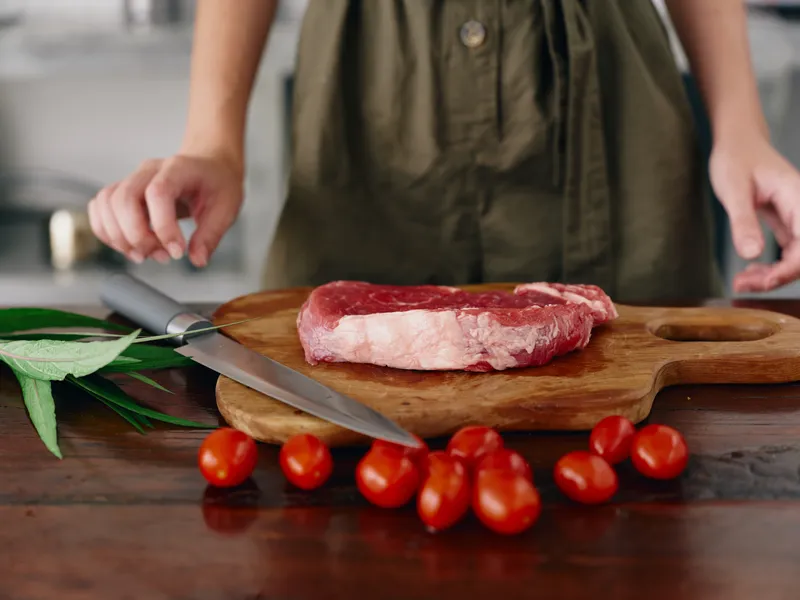 Женщина с ножом в руке нарезает свежее стейковое мясо для жарки на кухне