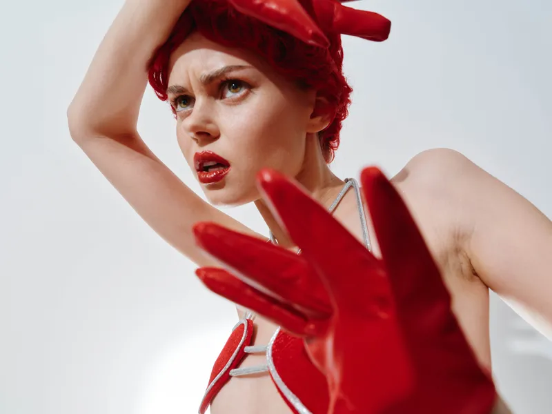 Женщина в красных перчатках и красной шапке держит руки на голове во время фотосессии в рамках зимней модной концепции