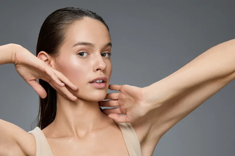 Young woman demonstrating skincare routine with glowing skin and a natural look in a neutral themed setting Focus on beauty and self care