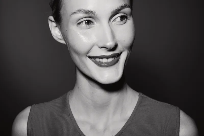 Close-up portrait of a smiling caucasian woman with fair skin and short hair looking sideways. Studio black and white photo with soft lighting and natural expression.
