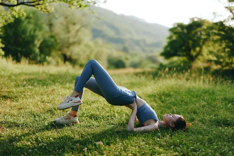 Young woman practicing yoga outdoors in a peaceful green field, showcasing flexibility and calmness in a seasonal spring setting