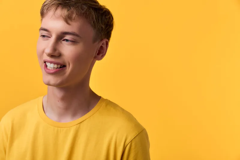 Smiling young man in a yellow tshirt against a bright yellow backdrop, casual and happy mood, friendly everyday scene with warm color