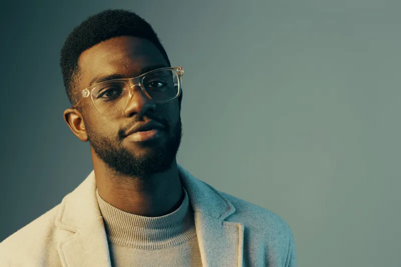 Stylish young African man with glasses posing confidently in a modern setting, showcasing contemporary fashion and vibrant color tones