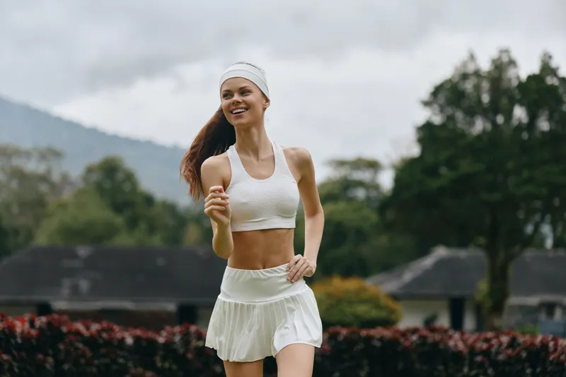 Happy athletic woman jogging in a beautiful outdoor setting, wearing white sportswear, promoting a healthy lifestyle and fitness