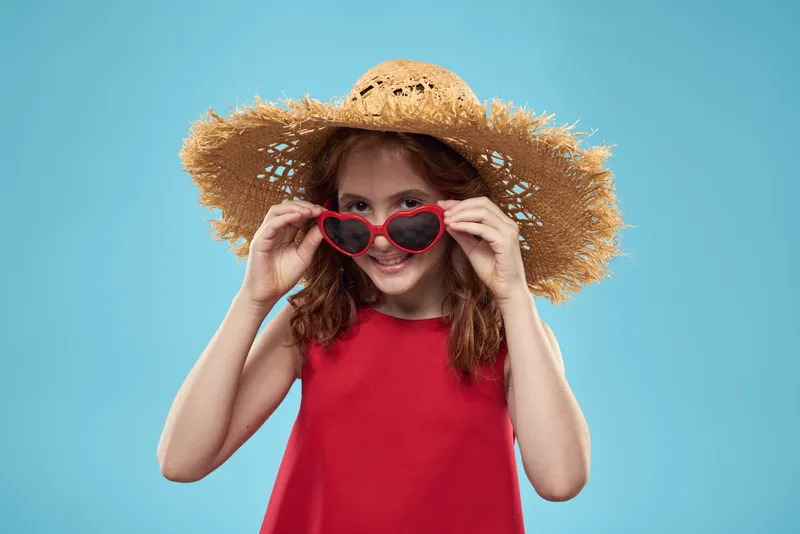 Девочка в соломенной пляжной шляпе, солнцезащитных очках, с кудрявыми волосами, веселье на голубом фоне