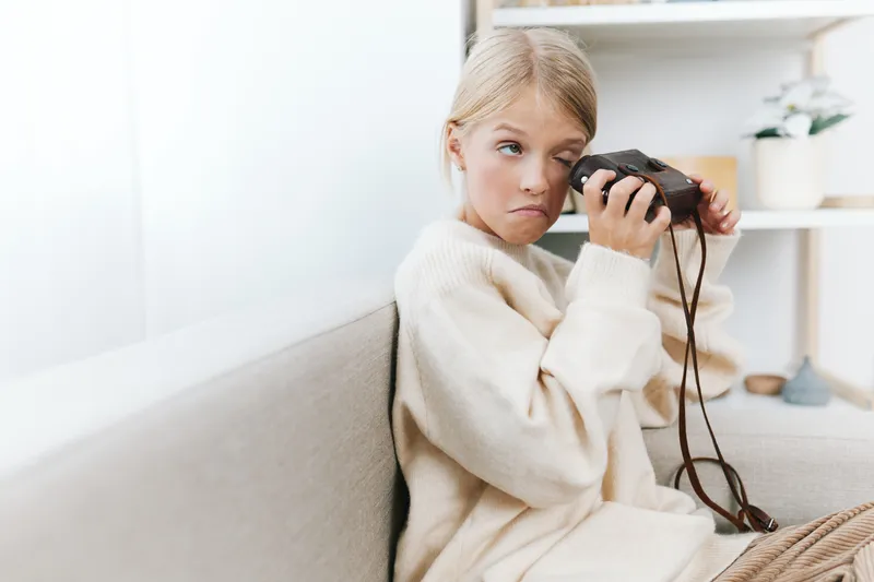 Authentic lifestyle shot of a young student at home with a vintage camera, capturing candid action and playful curiosity in a cozy setting.