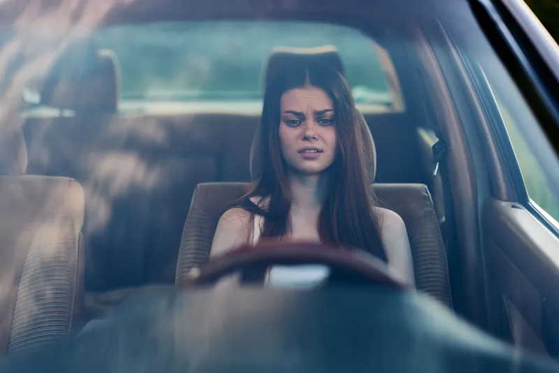 Young woman with long dark hair looking stressed while sitting in a car, showcasing raw emotions and a sense of confinement and anxiety.