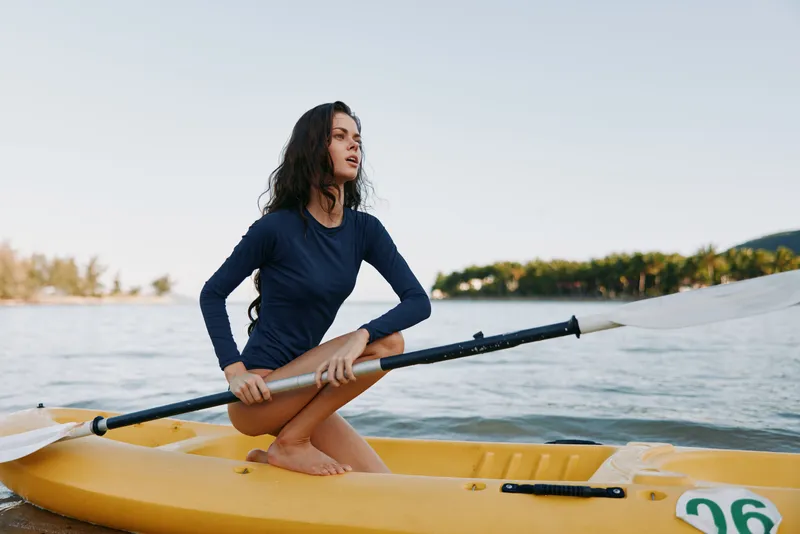 A young woman kneeling in a yellow kayak, gripping a double?bladed paddle as she paddles across calm water, showcasing balance, focus, and outdoor adventure.