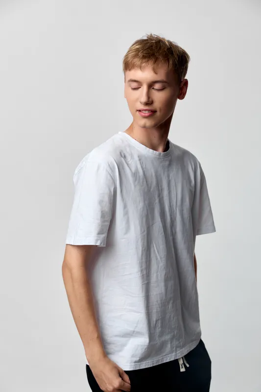 Man in a white tee with a relaxed pose against a neutral studio backdrop, showcasing casual fashion and effortless style, soft lighting and calm mood highlight simple everyday comfort