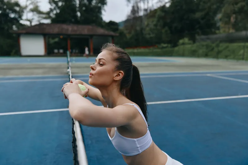 Young athletic woman enjoying a moment of relaxation on a tennis court, dressed in sporty attire, representing dedication to fitness and mental well being