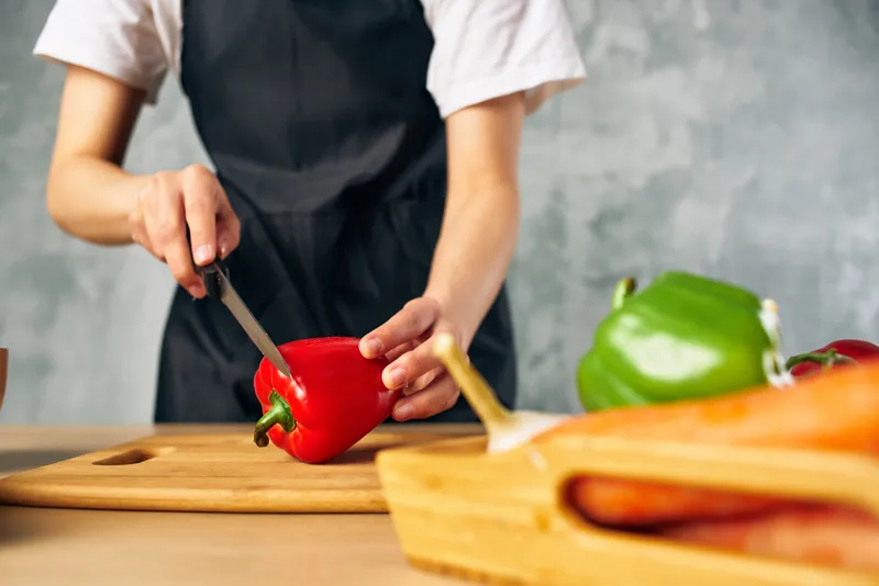 Женщина в черном фартуке на кухне нарезает овощи