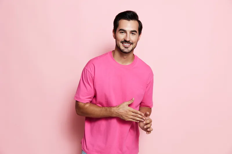 Smiling man in a pink t-shirt poses confidently against a solid pastel pink background, showcasing an approachable demeanor and friendly expression.