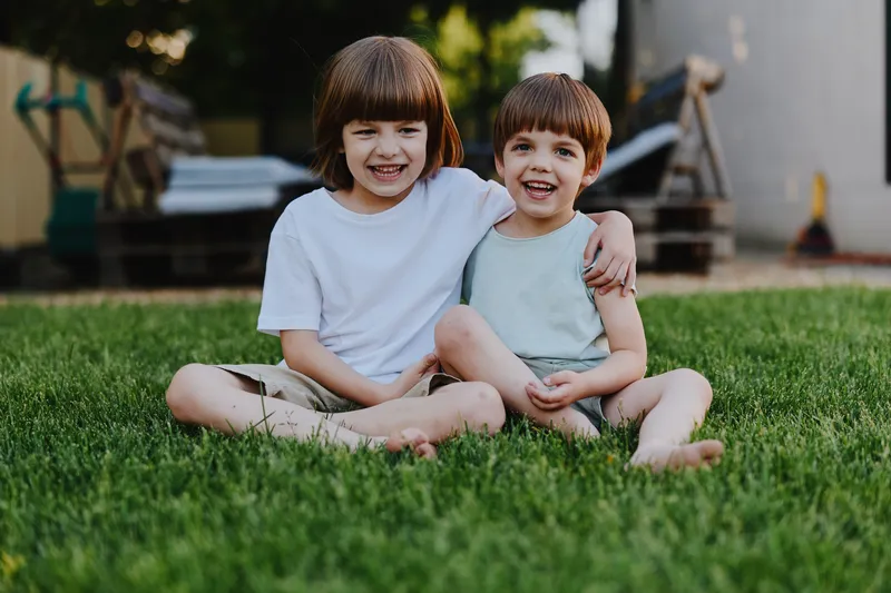 Happy children sitting on green grass, enjoying a sunny day while smiling and playing together in a cheerful outdoor setting, capturing moments of childhood joy.