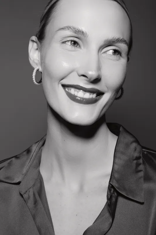 Smiling Caucasian woman with fair skin and short hair wears hoop earrings and a satin blouse. Close-up portrait in black and white studio lighting. Concept of beauty and elegance.