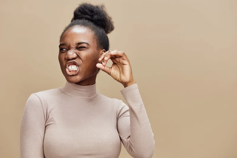 Joyful woman showing a gesture of excellence, wearing a beige turtleneck against a warm background, expressing confidence and pride