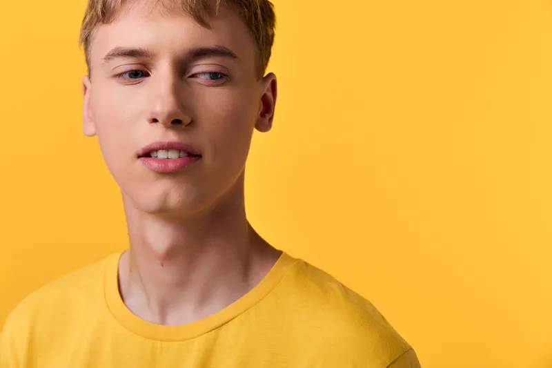 Young man in a yellow shirt with a soft expression against a bright backdrop, closeup on face and casual vibe for fashion, lifestyle and stock imagery