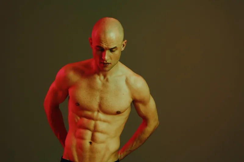 Athletic man posing confidently in a dramatic light setting, showcasing strength and determination with a stunning contrast of shadows and highlights.