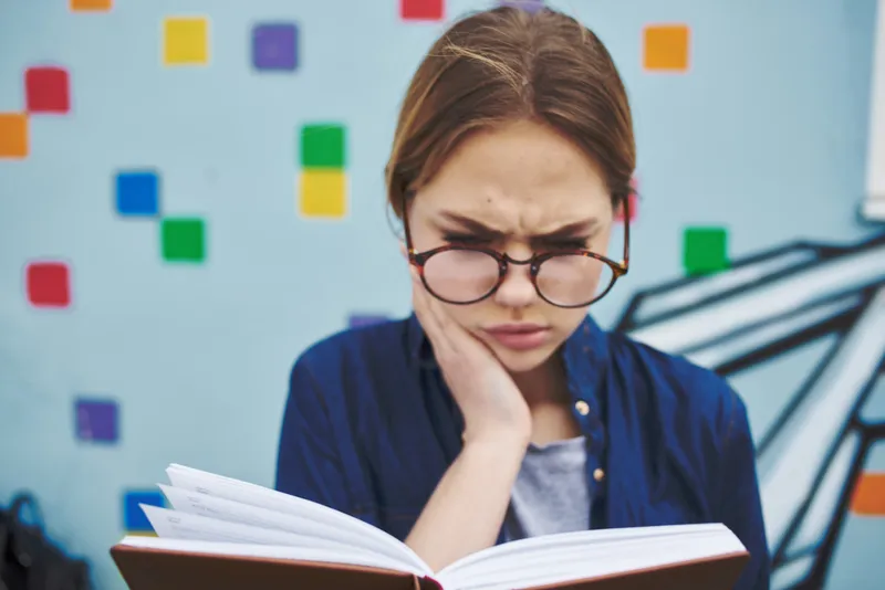 Удивленная студентка в очках на улице с книгой, эмоции, модель