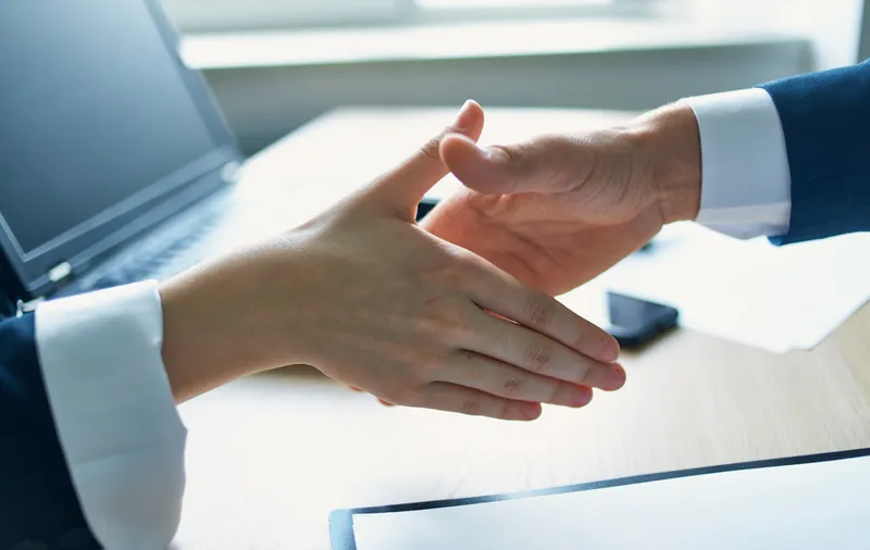 Сотрудники пожимают друг другу руки на работе в офисе, на столе лежат документы и ноутбук