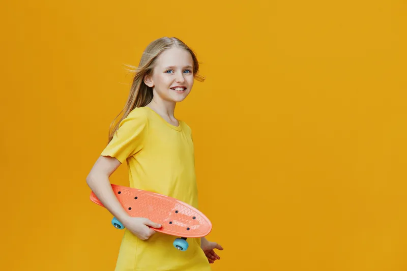 Cheerful girl with a skateboard in a vibrant yellow dress against a bright yellow background, embodying joy and energy in a playful summer scene
