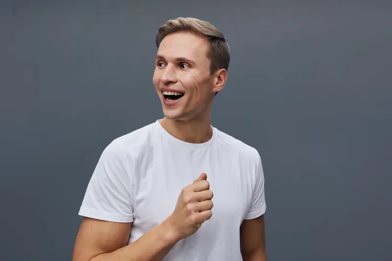 smiling young man wearing white t-shirt looking aside standing on gray background digital nomad lifestyle remote work concept