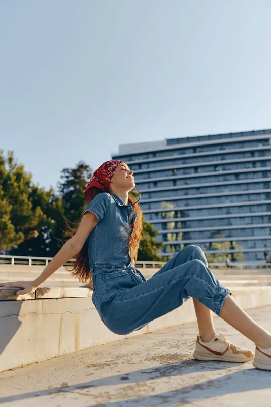 lifestyle woman in modern boho-western denim street style sitting outdoors with relaxed expression, film color tones and casual urban background