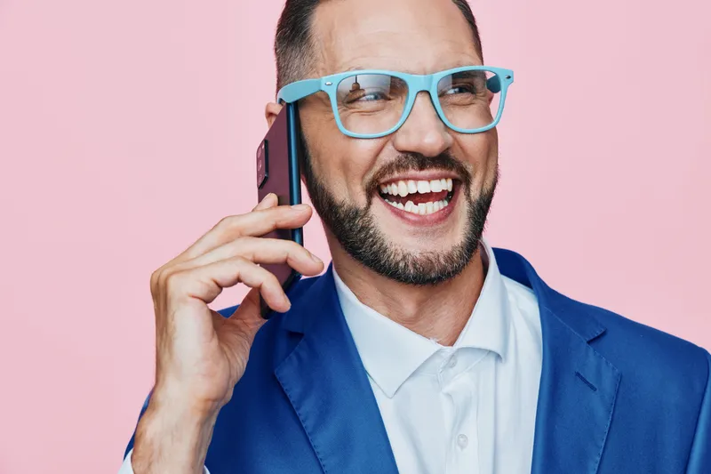 Professional man on phone with a bright smile, confident and energetic, portrayed against a solid pink background to emphasize business cheerfulness and dynamic mood.