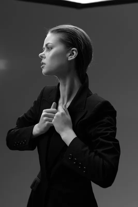 Black and white portrait of a serious woman adjusting blazer in studio lighting