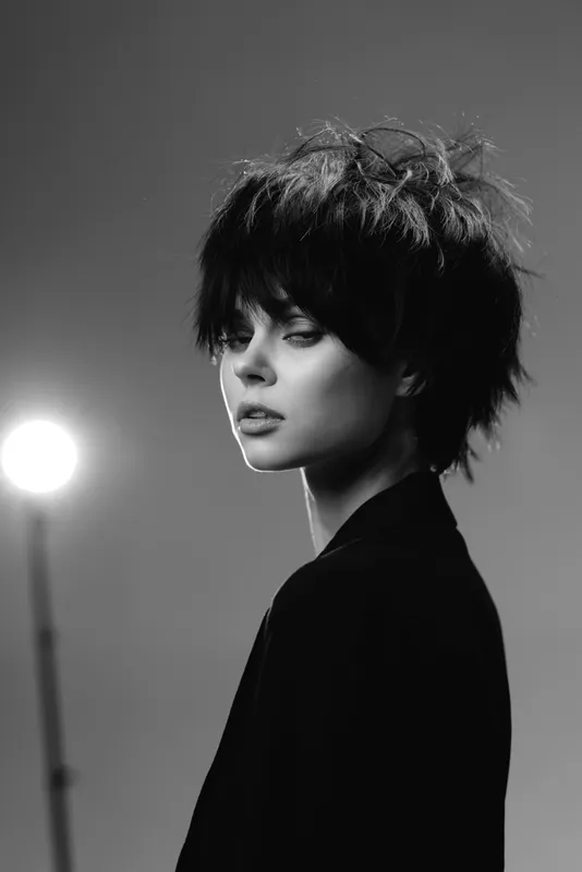 Black and white portrait of a young woman with short hair and expressive eyes in moody lighting.