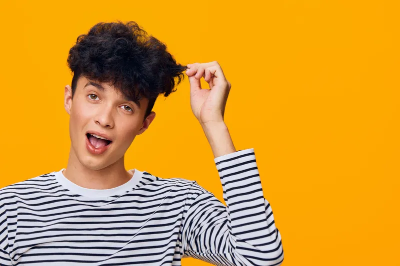 smiling young man in striped shirt with curly hair on bright orange background expressing surprise and joy, casual style, vibrant color, cheerful mood