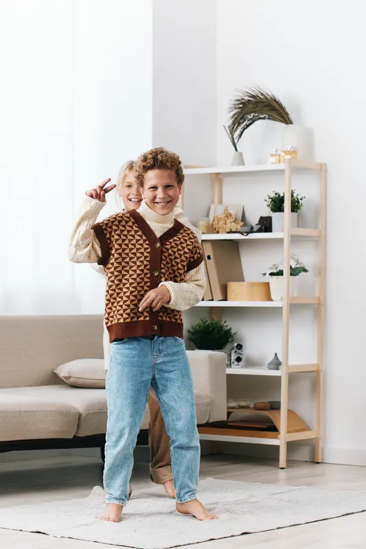 A joyful child dances indoors in a cozy living room, wearing a knitted vest and jeans, with an energetic pose and a bright smile, capturing playful energy and warmth.