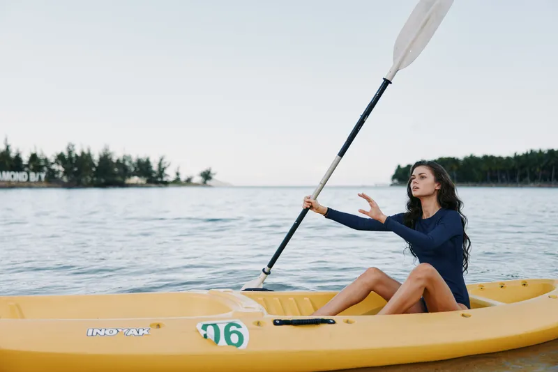 A young woman paddles a bright yellow kayak across calm lake water, focusing on rhythm and form as the paddle slices through the light spray.