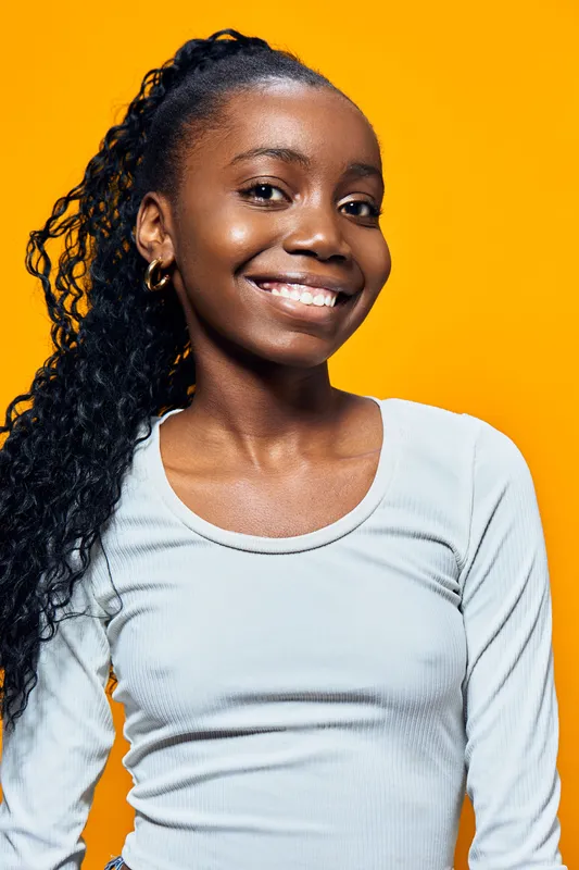 Cheerful girl with curly hair smiling against a bright yellow background, wearing a light blue top, capturing joy and positivity in a fun, vibrant concept