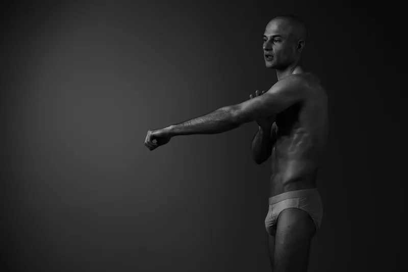 Black and white portrait of a man stretching confidently, showcasing his physique and strength in an artistic manner. Ideal for fitness and wellness themes.