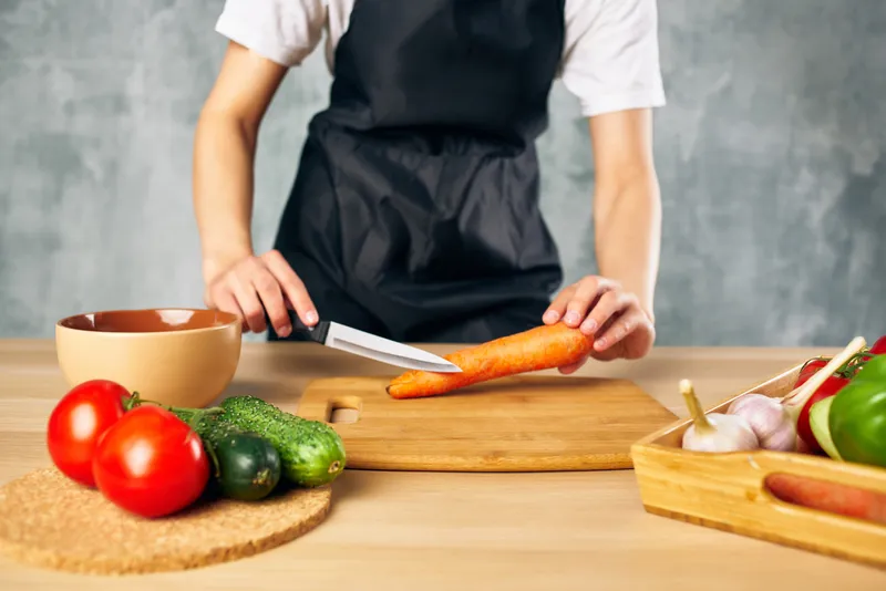 Женщина в черном фартуке на кухне нарезает овощи
