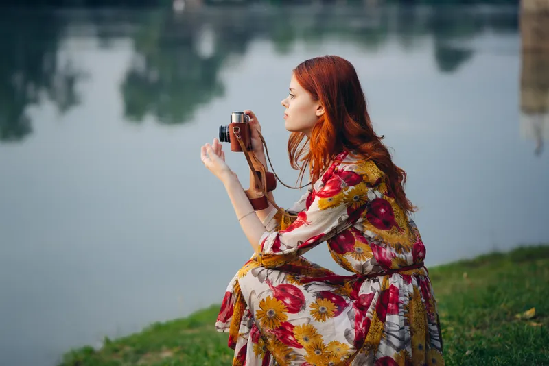 Женщина в платье с фотоаппаратом на природе, фотографирует реку, хобби